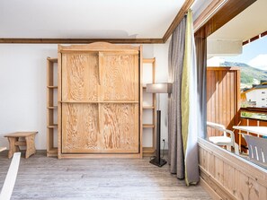 A room with a wooden wardrobe, a floor lamp, and a view of the outside.