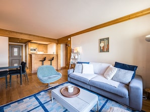 A living room with a sofa, a chair, a coffee table, a kitchen area, and a door. - Charming apartment, ski-in/ski-out, parking included (Val-d'Isère)