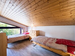 A cabin with two wooden beds, a dresser, and a window overlooking a forest.