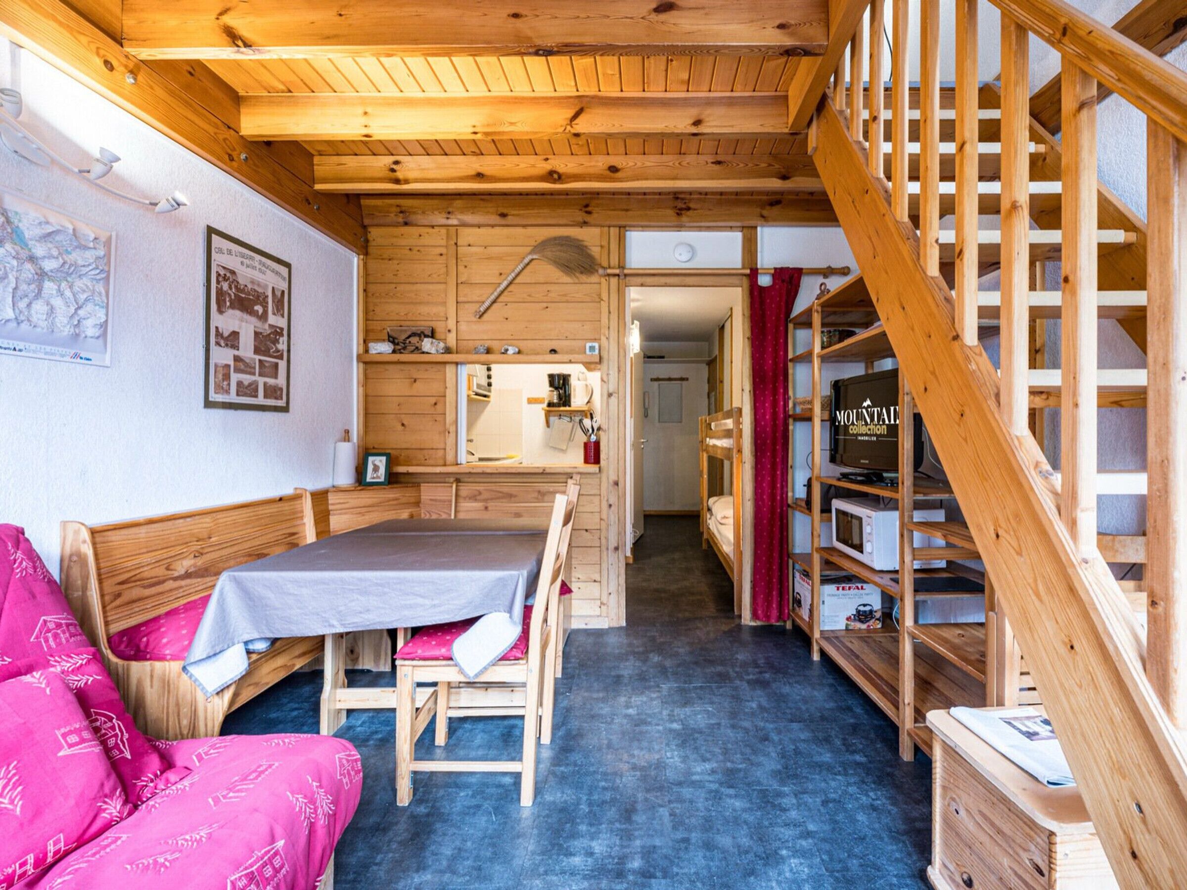 Ein Holzinnenraum mit einem Etagenbett, einem Tisch mit Tischdecke, einem Regal mit Fernseher und einer Treppe.