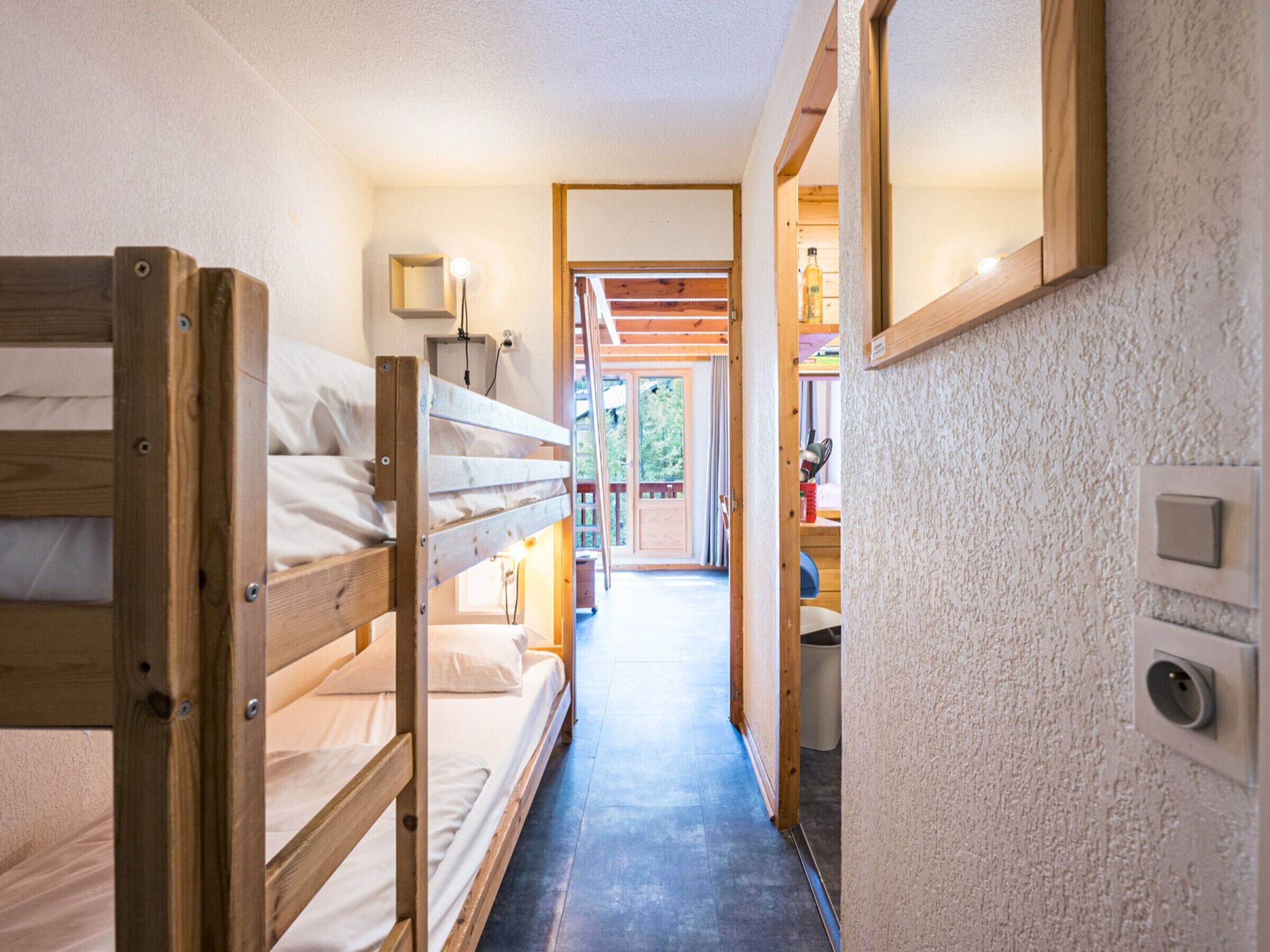 A narrow hallway with bunk beds on one side and a door leading to a room with a window.