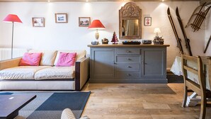 A cozy living room with a sofa, a wooden cabinet, a dining table, and skis leaning against the wall.