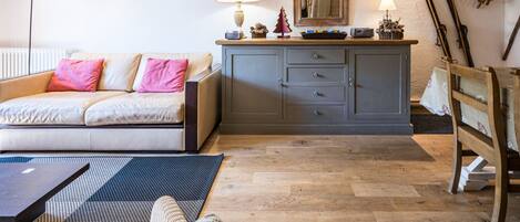 Een gezellige woonkamer met een bank, een houten kast, een eettafel en ski’s die tegen de muur staan.