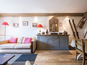 A cozy living room with a sofa, a wooden cabinet, a dining table, and skis leaning against the wall.