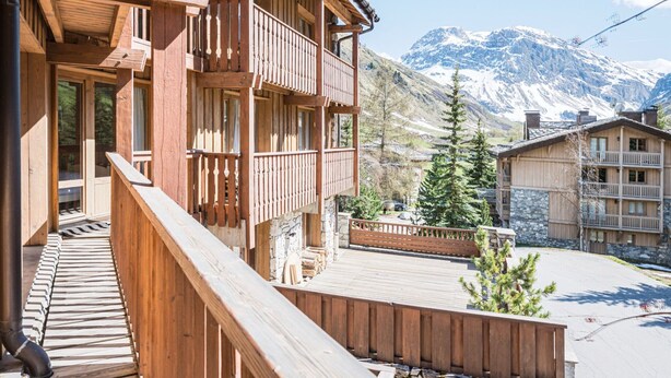 A wooden building with balconies, a stone facade, and a mountainous backdrop.