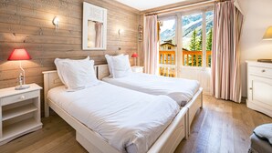 A bedroom with two beds, wooden walls, a window with curtains, and a view of a mountain. - Cozy 3-bedroom apartment with direct piste access in Val-d'Isère (Val-d'Isère)