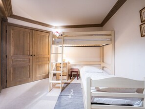Habitación con literas, un armario de madera, una mesita de noche pequeña y una lámpara.