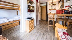 A compact room with a bunk bed, a wooden dresser, a desk with a chair, a television, and a kitchen area with a microwave and toaster. - Renovated Studio Cabin - Ski-in/Ski-out - WIFI (Val-d'Isère)