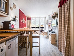 A compact kitchen with a wooden table, a refrigerator, a microwave, and a television on a stand.