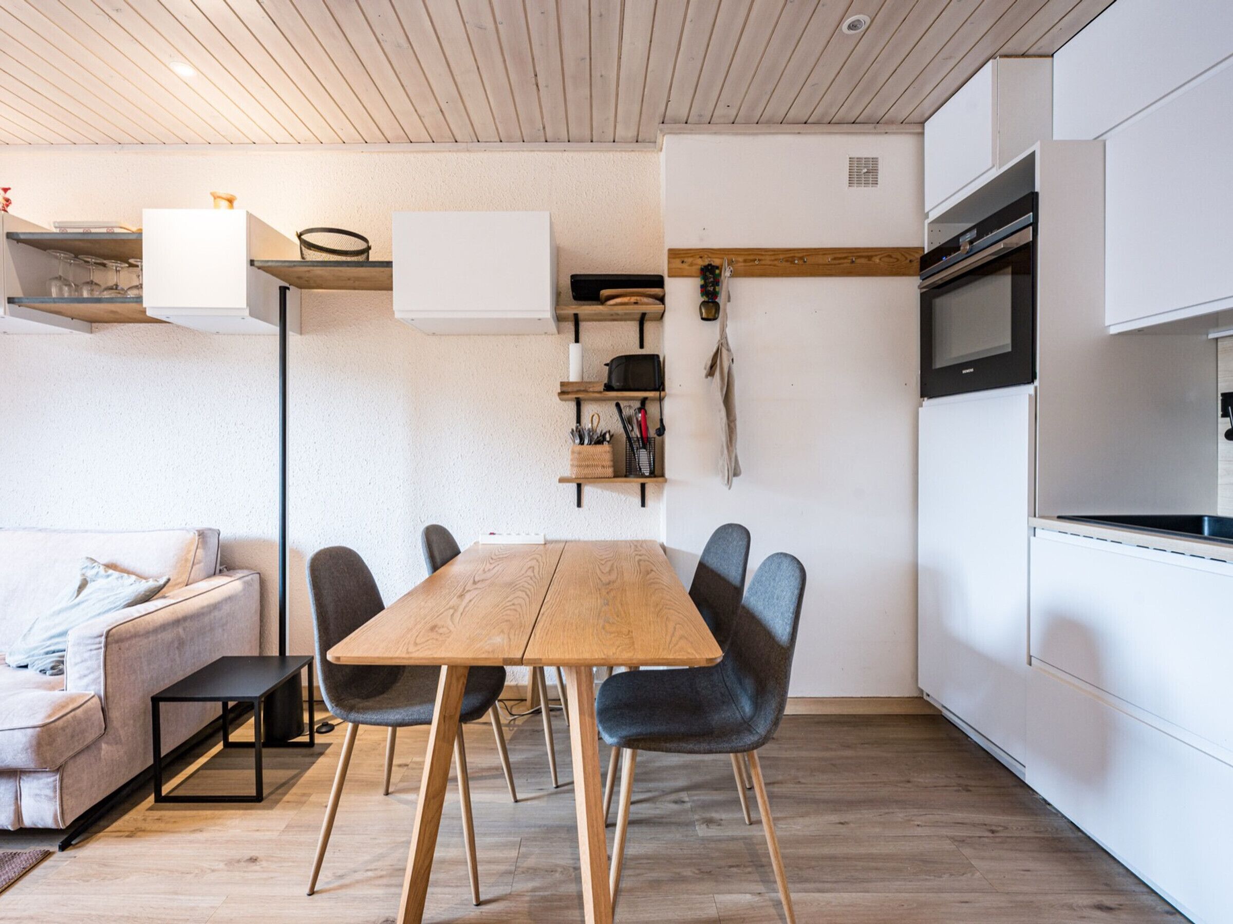 Une cuisine moderne avec une table et des chaises en bois, un four encastré et un plan de travail blanc.