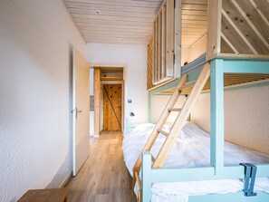 Corredor estreito que leva a uma porta de madeira, uma cama beliche com escada e piso de madeira.