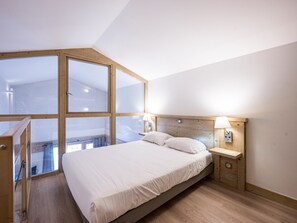 A bedroom with a large window, a bed, bedside tables, and a wooden headboard.