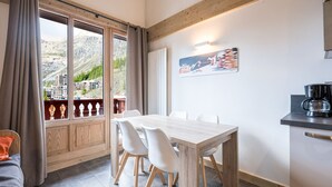 A dining area with a wooden table and chairs, a view of a mountainous landscape through a large window, and a painting on the wall.