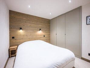 Quarto com painel de parede em madeira, uma cama, duas luminárias na parede, um guarda-roupa e uma pequena mesa de cabeceira.