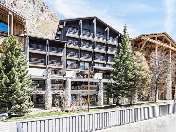 A multi-story hotel with balconies, stone pillars, and a mountain backdrop.