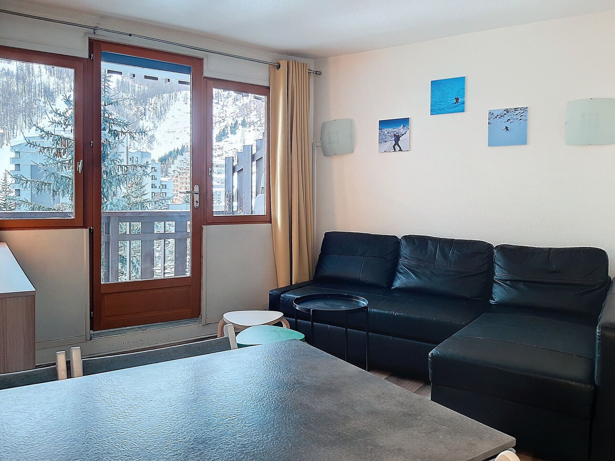 A room with a black leather sofa, a small round table, and a window with a view of snow-covered trees and buildings.