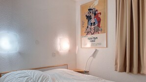 A bedroom with a bed, a wall-mounted light, and a poster.