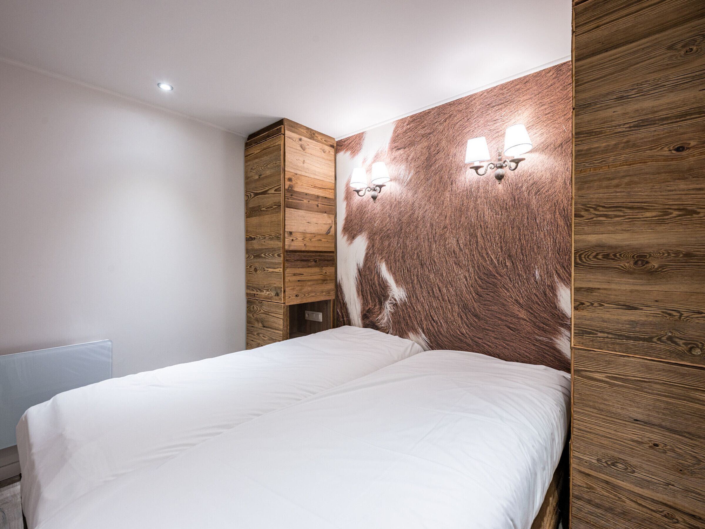 Une chambre à coucher avec une tête de lit en bois, un lit blanc et deux lampes fixées au mur.
