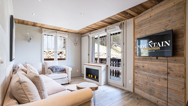 A modern living room with a sofa, fireplace, wooden walls, and a television displaying 'MOUNTAIN collection'. - Renovated apartment, ski-in/ski-out, includes parking (Val-d'Isère)
