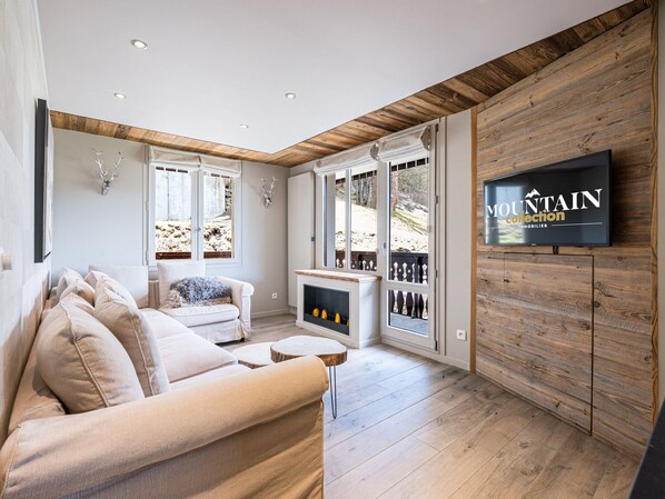 A modern living room with a sofa, fireplace, wooden walls, and a television displaying 'MOUNTAIN collection'.