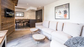 A modern interior with a sofa, wooden flooring, a kitchen area, and a mounted television. - Renovated apartment, ski-in/ski-out, includes parking (Val-d'Isère)