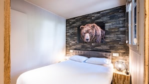 A bedroom with a large bed, a stone wall, and a bear picture. - Renovated apartment, ski-in/ski-out, includes parking (Val-d'Isère)
