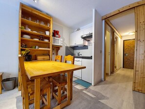 Una cocina compacta con una mesa y sillas de madera, estante empotrado con vajilla, microondas y lavavajillas.