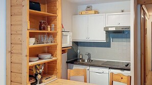 Una cocina compacta con gabinetes blancos, microondas, lavavajillas y una mesa de madera.