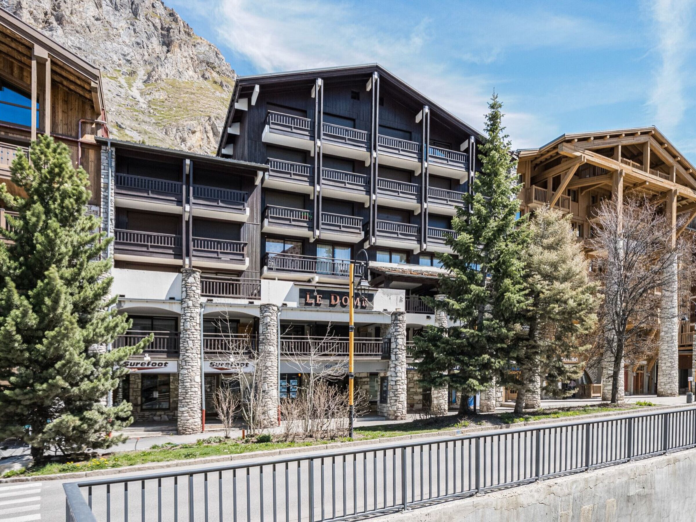 A multi-story hotel with balconies, stone pillars, and a ski resort backdrop.