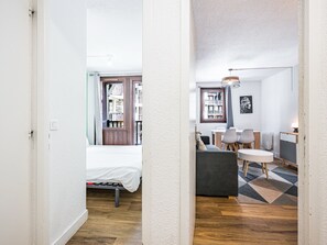 Un couloir étroit mène à une chambre à coucher équipée d’un lit et d’une fenêtre, ainsi qu’à un petit coin salon avec une table et des chaises, et une bibliothèque.