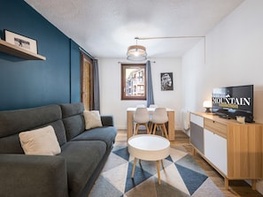 Un salon moderne avec un canapé, une table à manger, des chaises, un téléviseur et une vue sur la rue par une fenêtre.