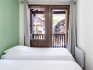 A bedroom with a bed, a window with curtains, and a view of buildings.