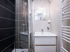 Ett modernt badrum med en dusch med glasväggar, en vit tvättställ och en handduksställning.