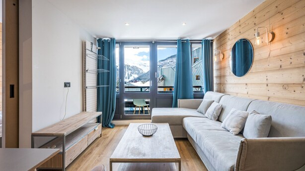 Un salon moderne avec un canapé, une table à manger et une vue sur les montagnes grâce à de grandes fenêtres.