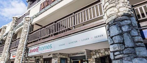A two-story building with a stone facade and a balcony. The ground floor has a sign for 'Sweethomes' with a 'VENDRE - ACHETER - LOUER - GERER' sign above it.