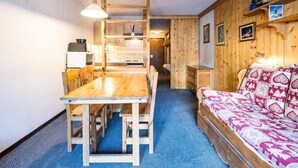 A compact room with a wooden dining table, a sofa with patterned cushions, a kitchenette, and a bunk bed. - Comfortable studio in center, balcony, 2-3 pers. (Val-d'Isère)