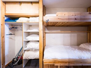A bunk bed room with a wooden bunk bed, a shelf with folded clothes, and a vacuum cleaner on the floor.