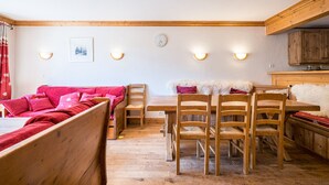 A cozy room with a wooden bed, a red sofa, a dining table with chairs, and a kitchen area with wooden cabinets.