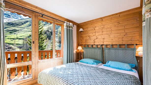 A bedroom with a large window, wooden walls, a bed with checkered bedding, and two bedside lamps.