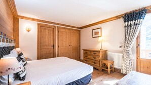 A bedroom with a bed, wooden wardrobe, dresser, and a window with curtains.