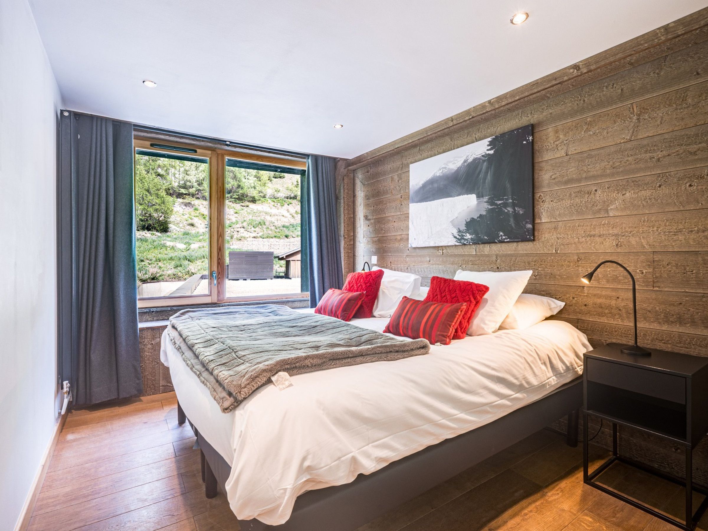 Een moderne slaapkamer met een groot bed en uitzicht op groen, met een houten wand.