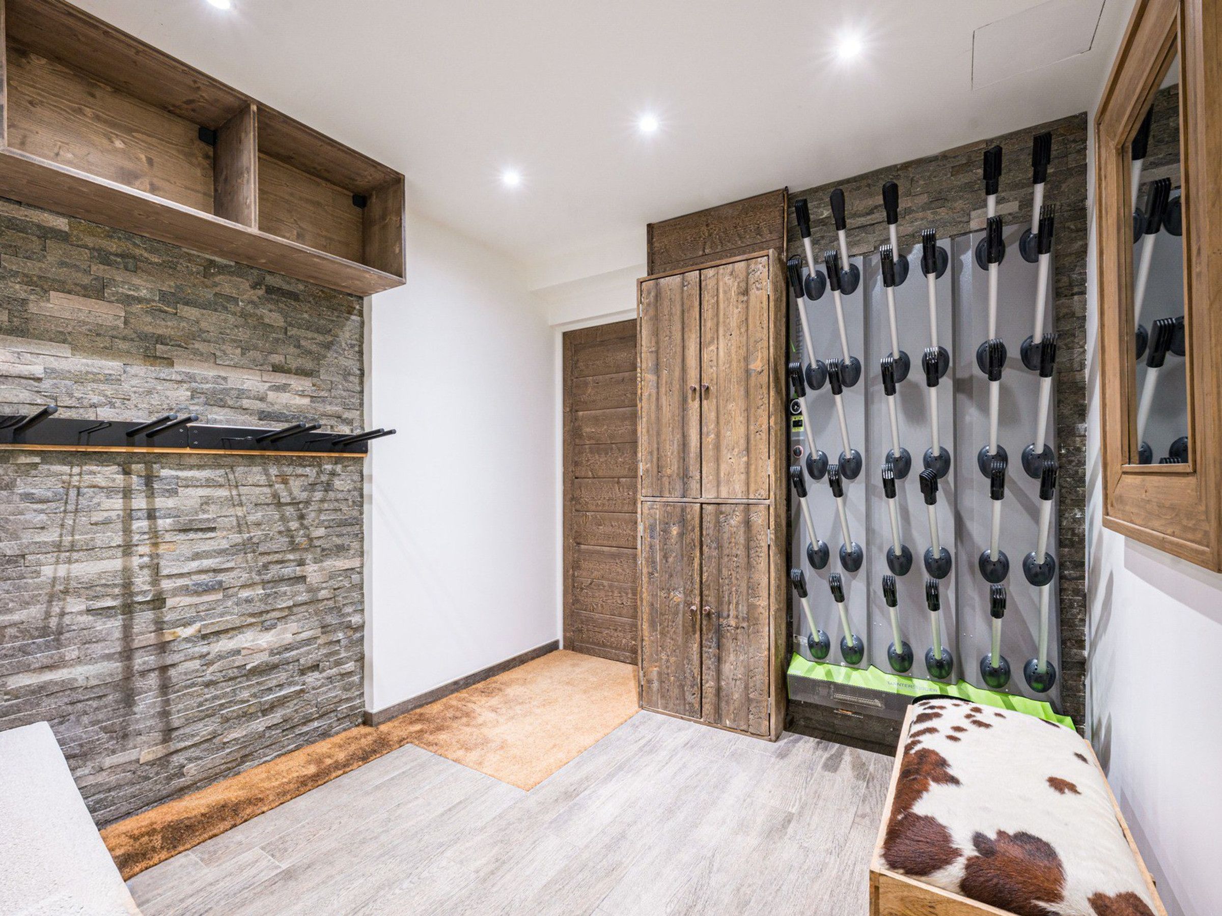 A room with a stone wall, wooden shelves, a wardrobe, and a mirror with a wooden frame.