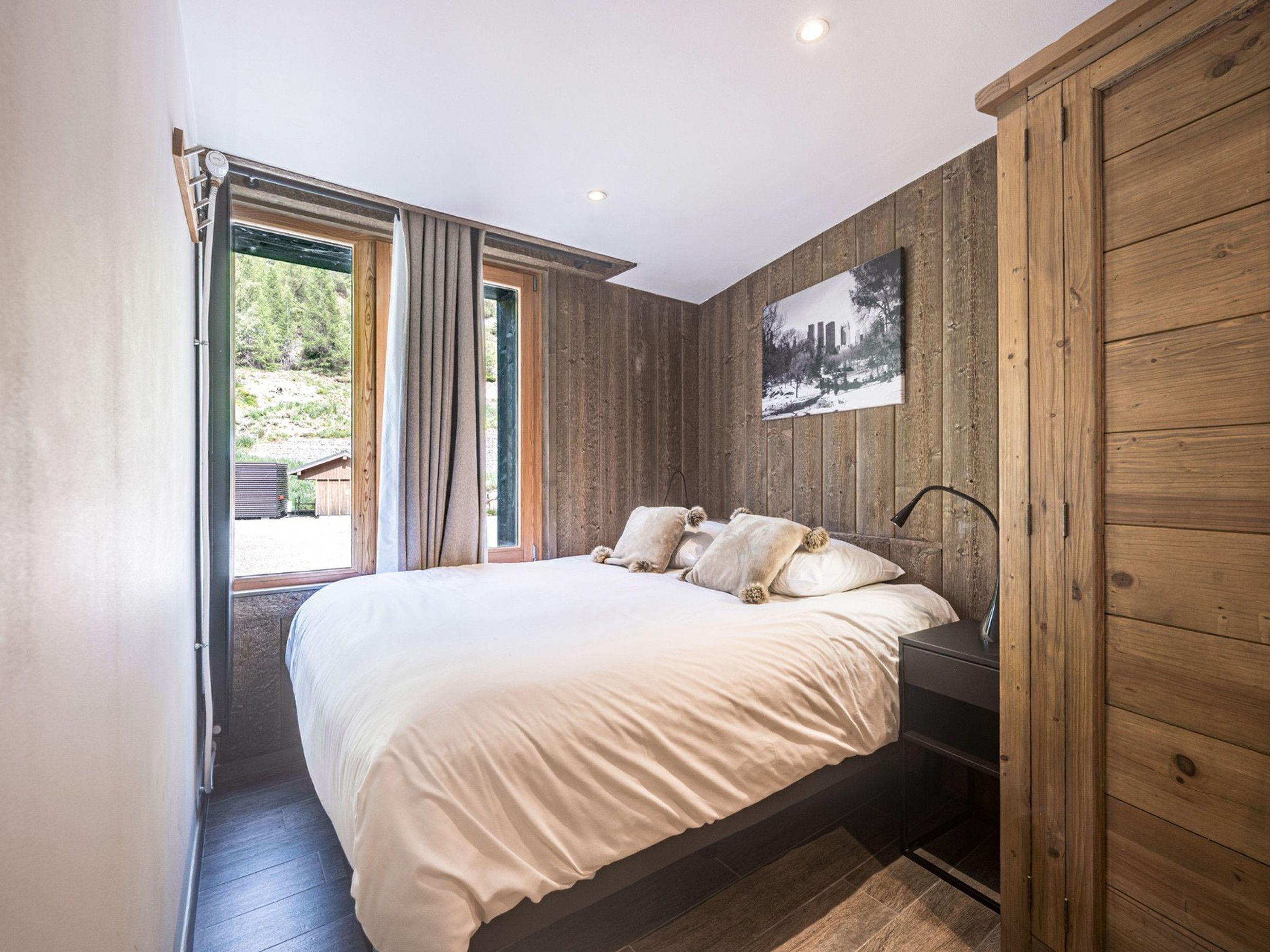 Un dormitorio con una cama grande, paredes de madera, una ventana y una puerta que da al exterior.