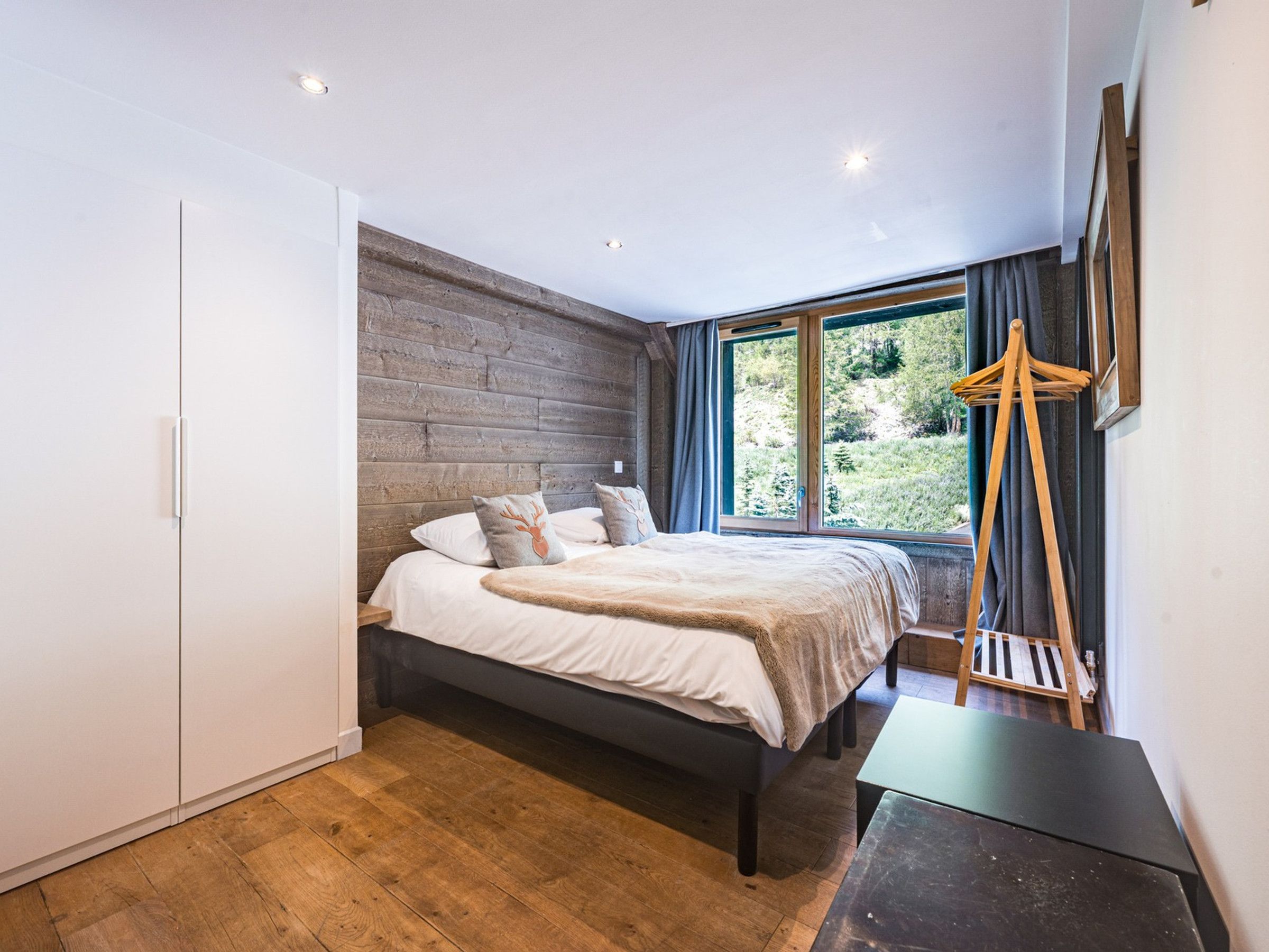 Een slaapkamer met een bed, een kledingkast, een raam met uitzicht op groen en een houten vloer.