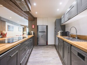 Cozinha moderna com geladeira de aço inoxidável, bancadas de madeira e armários cinzas.