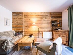 A cozy living room with a wooden wall, a sofa, a coffee table, a lamp, a television, and a cabinet. - Renovated apartment with slope access and covered parking (Val-d'Isère)