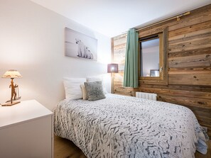 A bedroom with a bed, a nightstand, a lamp, a painting, and a window with curtains. - Renovated apartment with slope access and covered parking (Val-d'Isère)