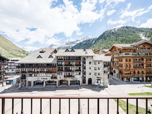 A multi-story hotel with stone and wooden facades, balconies, and a view of snow-capped mountains.