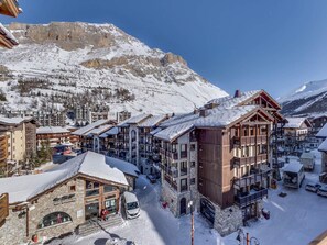 Una località montana innevata con edifici in legno, una seggiovia e un cielo azzurro limpido.