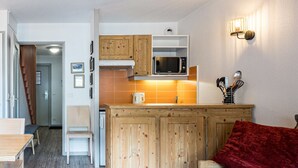 A compact living space with a kitchenette, wooden cabinets, a microwave, a dining area, and a sofa with a red cushion.